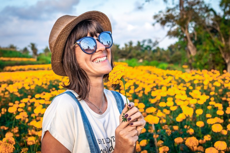 Happy white woman in a straw hat amongst a field of yellow flowers