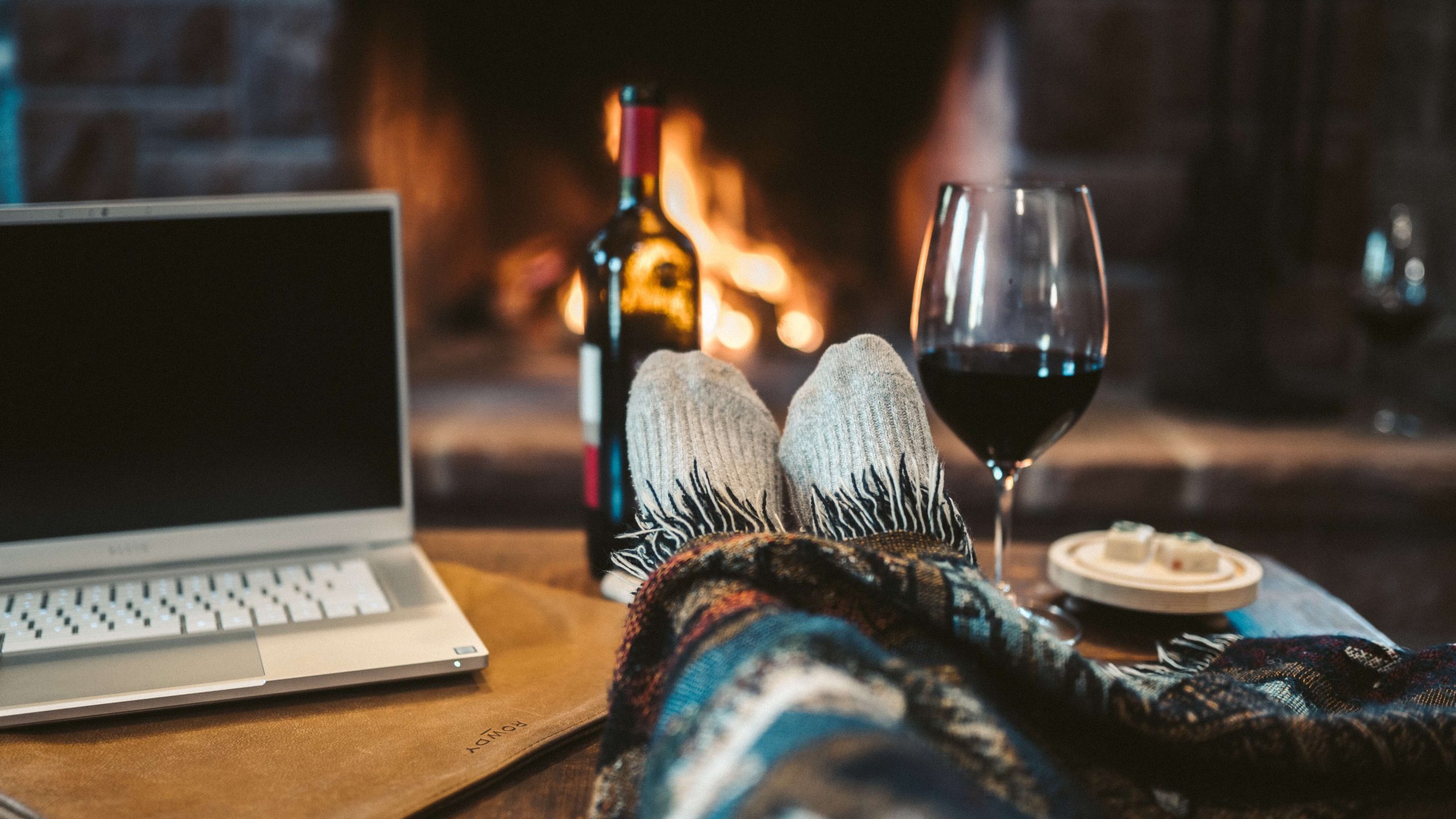 Feet in warm socks and a glass of wine on a table in front of an open fire